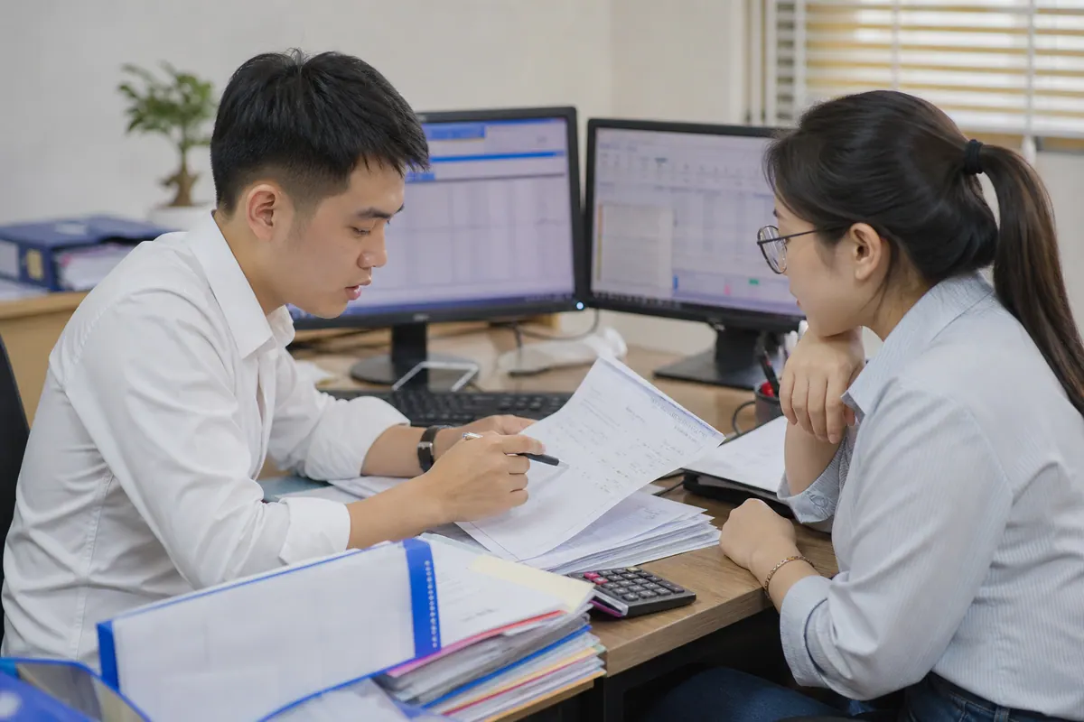 Kế toán viên trẻ kiểm tra kết quả phân tích trên máy tính với chứng từ và đồng nghiệp